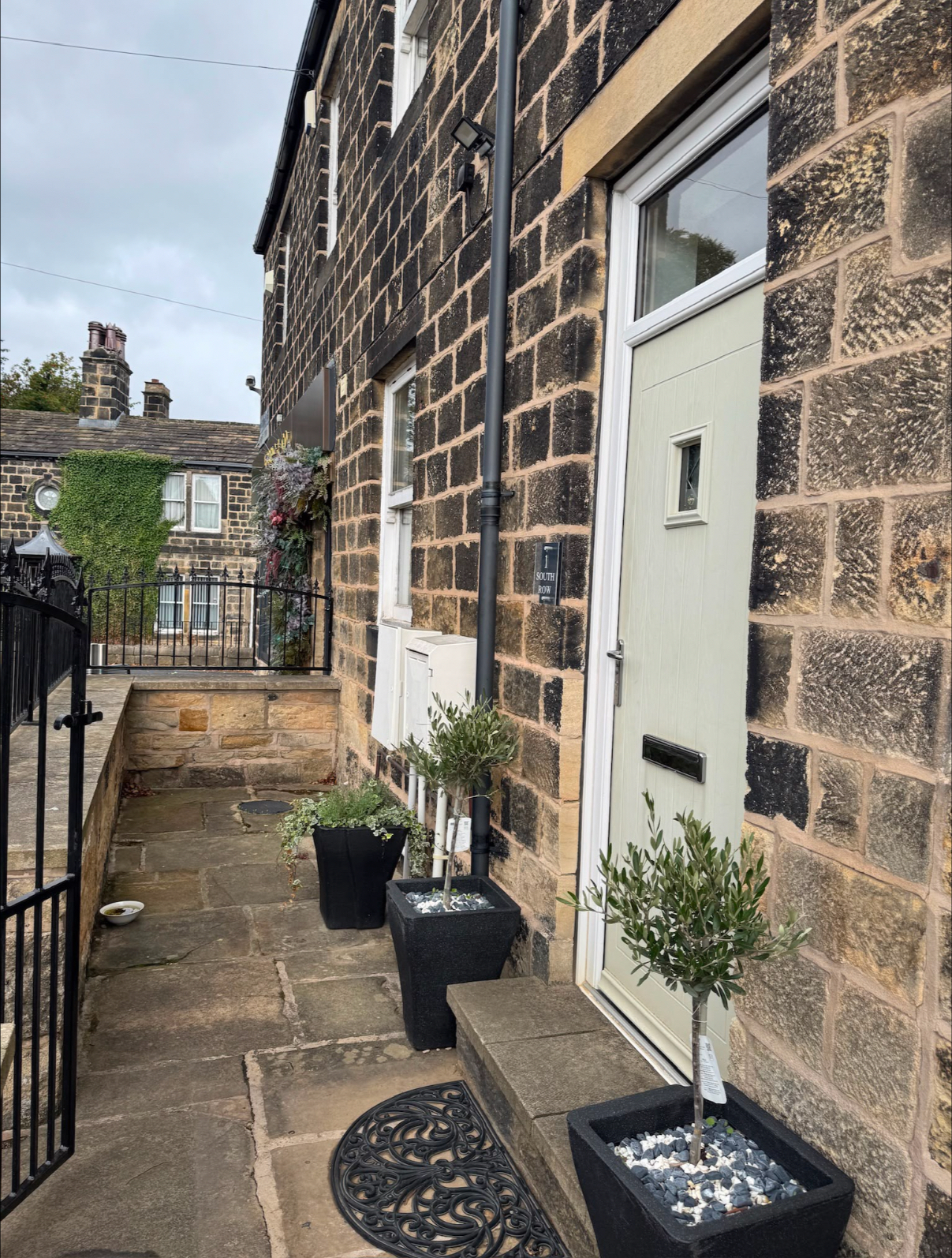 The green side door beside the stone building, with potted olive trees outside